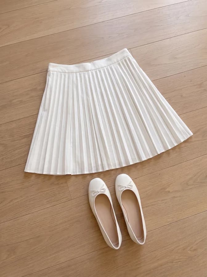 Foto de celular de la pollera plisada blanca y las chatitas, sobre el mismo piso