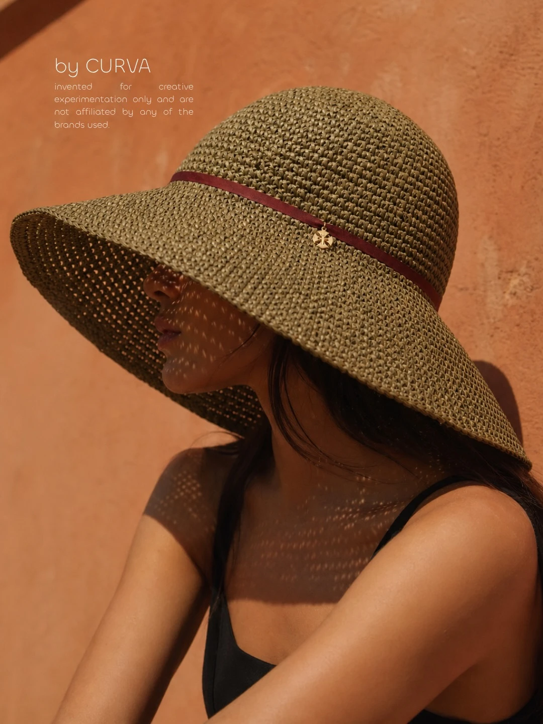 Modelo de perfil con sombrero de rafia verde oliva de ala ancha, cinta bordó y dije dorado, musculosa negra, contra una pared terracota al sol