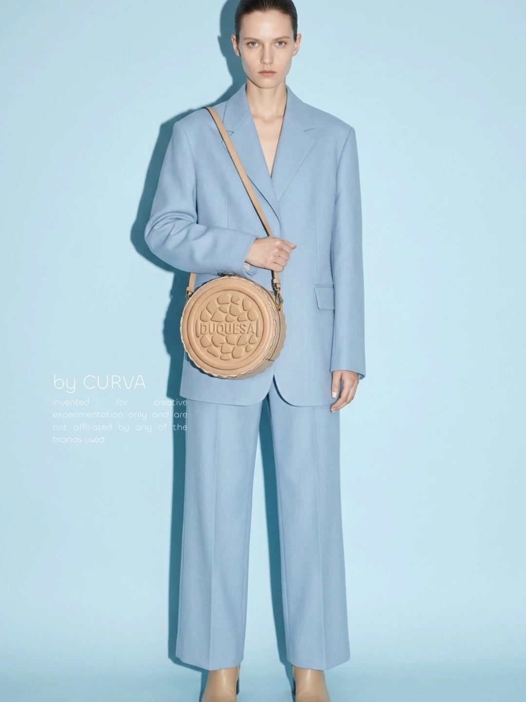 Modelo con traje sastrero celeste de saco y pantalón amplio, con bolso circular beige con forma de galletita, sobre fondo celeste